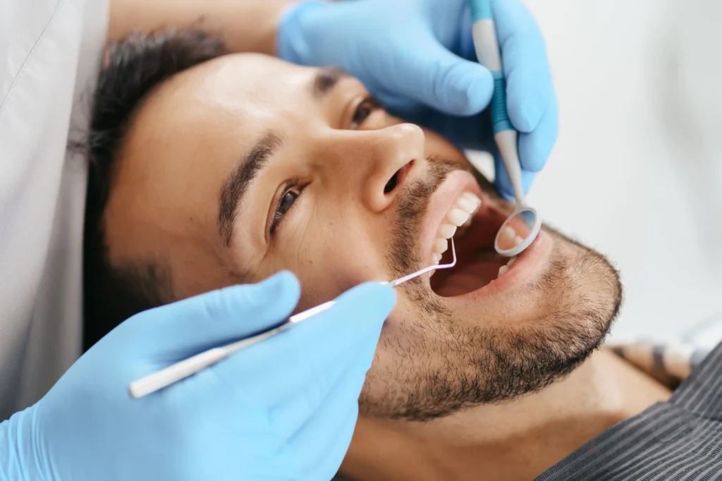 smiling-young-man-sitting-dentist-chair-while-doctor-examining-his-teeth-1-1-scaled